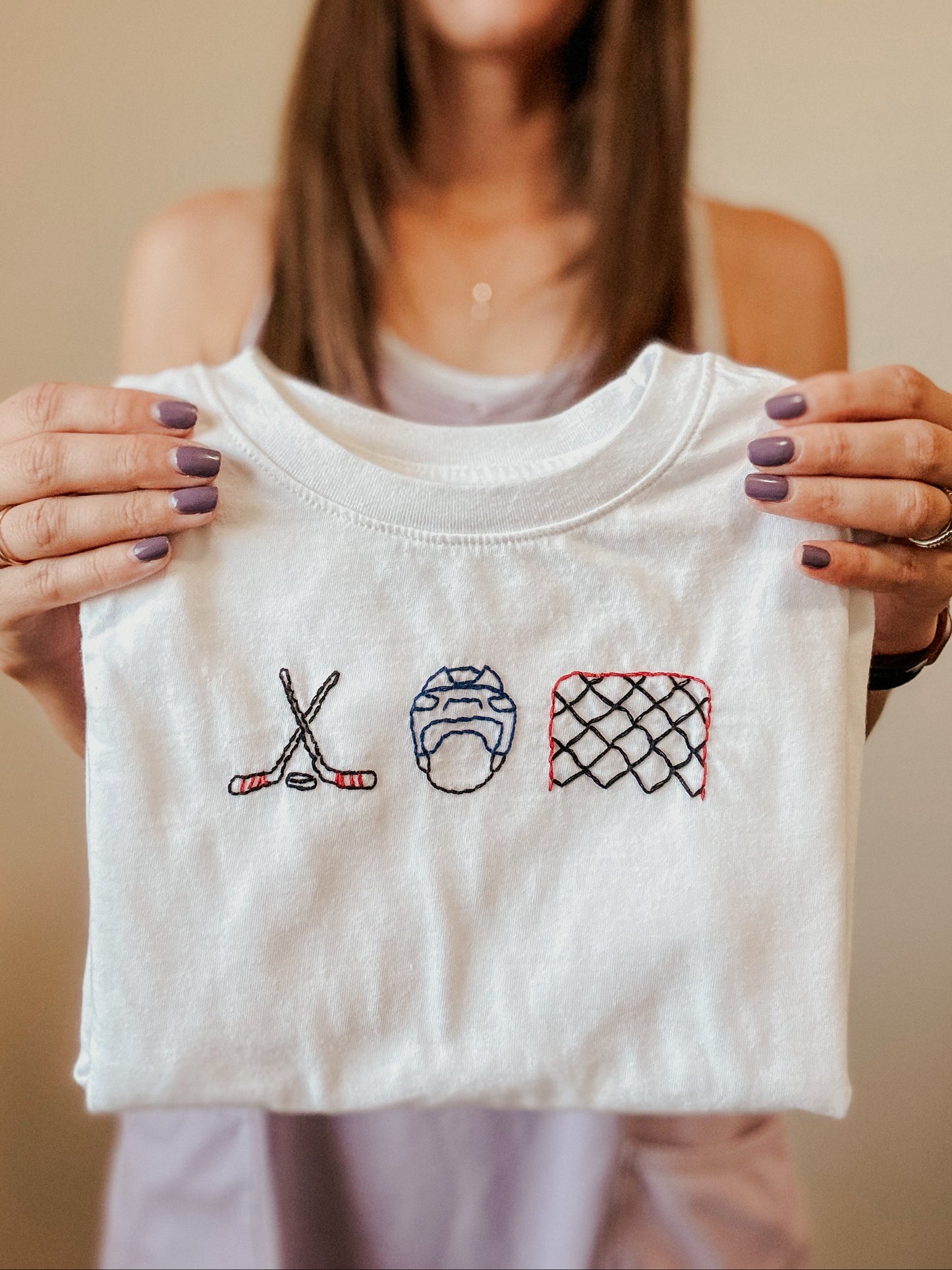 Person holding a white tshirt with hockey-themed embroidery.